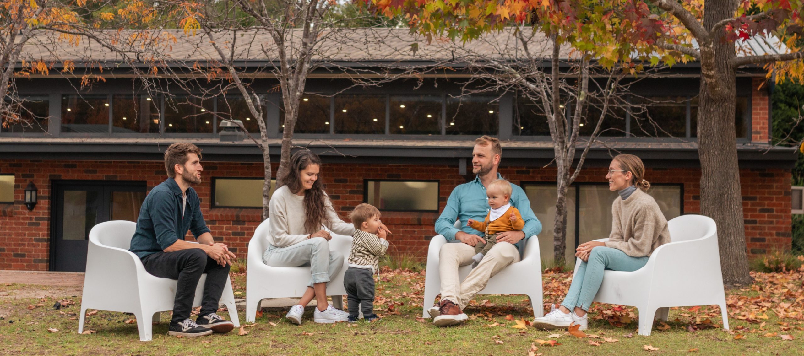 Two couples at a group accommodation venue sit with their toddlers in an outdoor communal space.