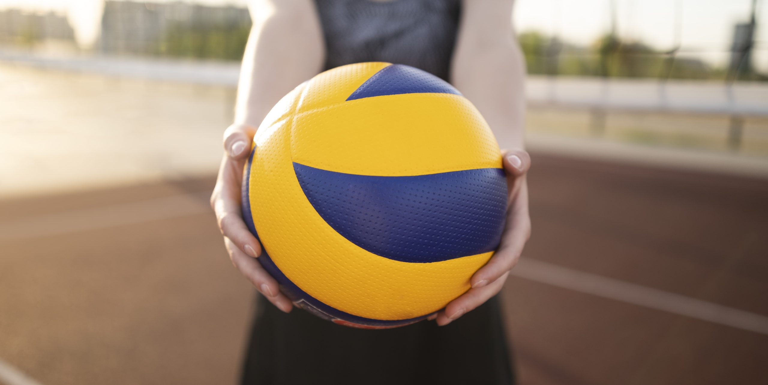 A girl holds out a yellow and blue volleyball