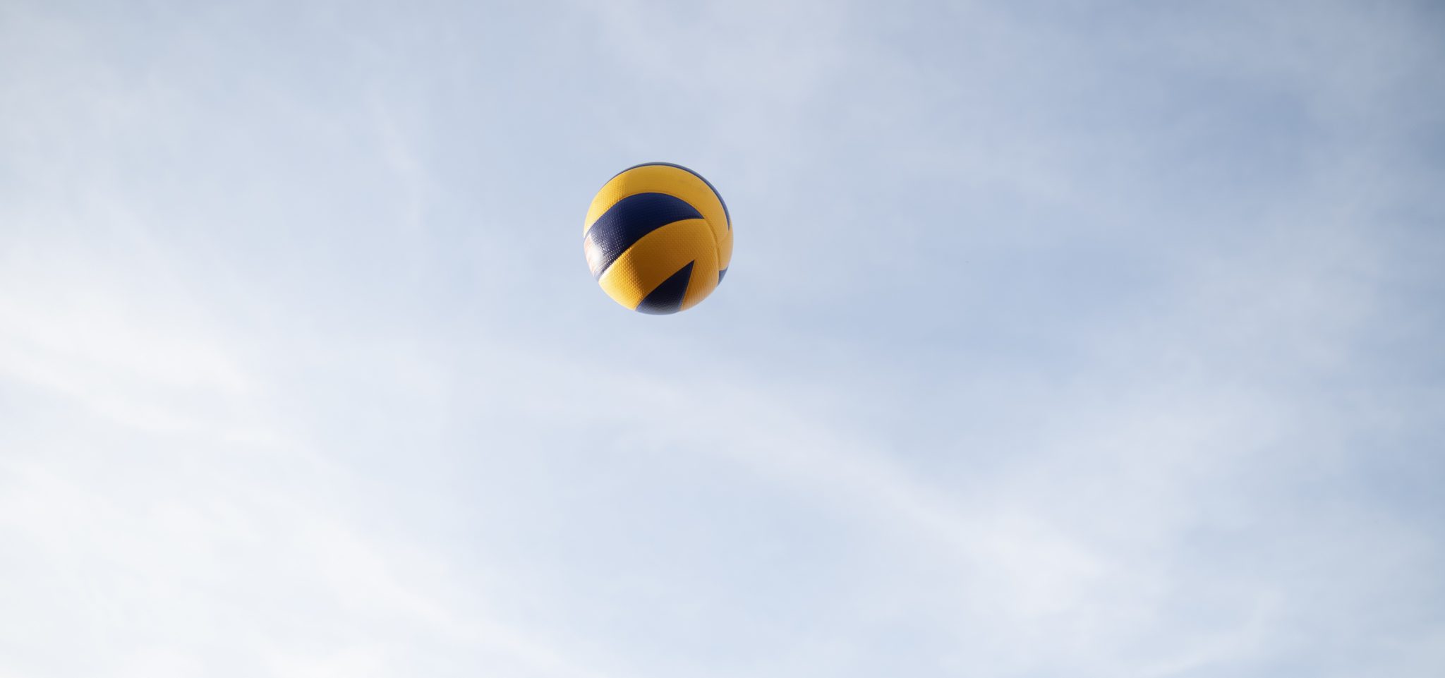 A volleyball flying through the air against a sunny, blue sky